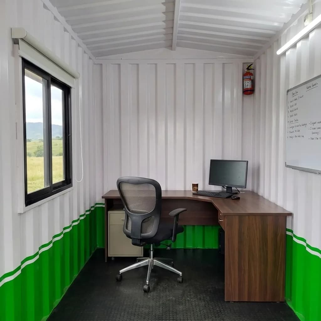 Interior of the 10 × 10 ft portable office cabin fitted with an L-shaped desk, chair and whiteboard