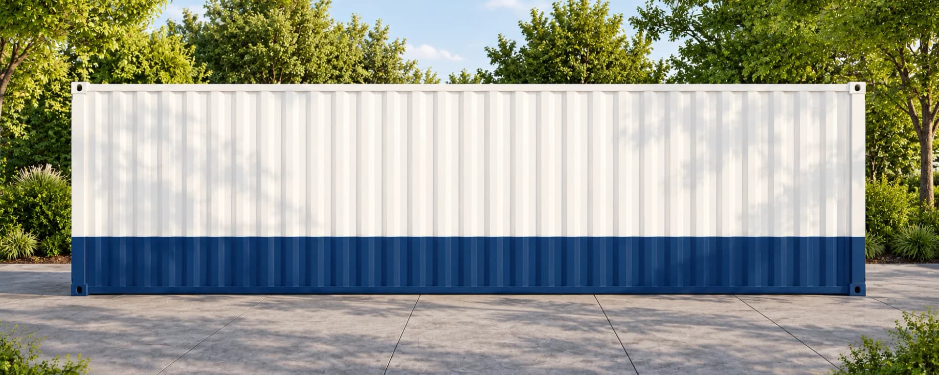 Long plain side of an office cabin clad in corrugated steel, painted white above a navy lower band, standing on a paved yard with trees behind