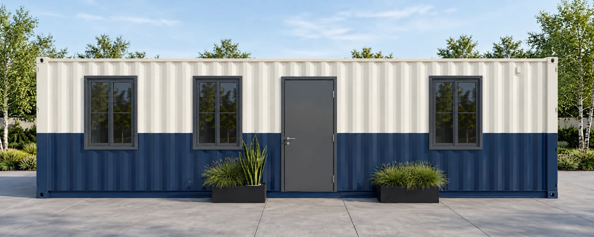 Long white and navy office cabin clad in corrugated steel, with a grey entrance door, two dark-framed windows to its left and one to its right, and two planters in front, on a paved yard